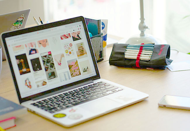 Zu sehen ist ein Laptop, der auf einem Tisch steht und den Pinterest-Homefeed zeigt. Es geht um die Frage „Was ist Pinterest?“. Bild: Unsplash / Eugene Chystiakov
